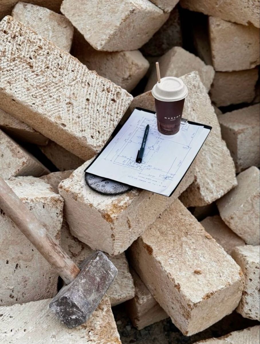 Site plans, coffee and a pen resting on a stack of bricks