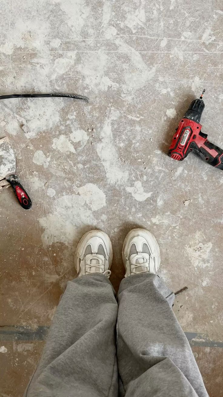 Boots, a drill and a scraper on a dusty job site floor